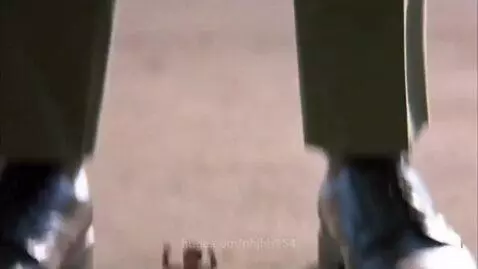 A tiny man stands between the large black boots of a soldier in uniform, trying to get his attention.