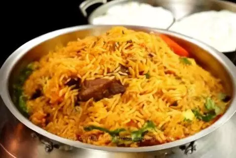 Steaming pot of Hyderabadi mutton dum biryani with basmati rice and garnishes.