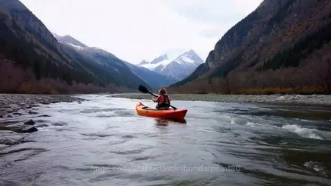 Kayaker in orange kayak paddling down a fast-moving river through a mountain valley.