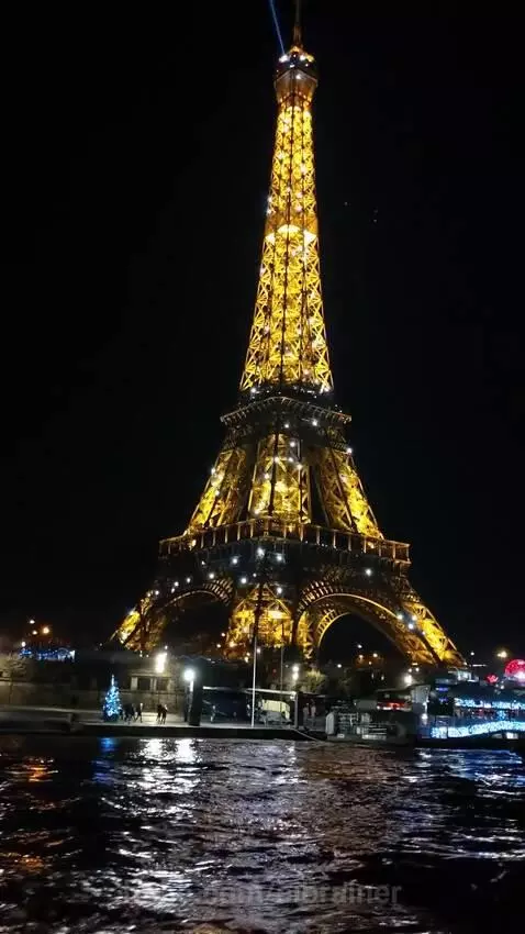 Eiffel Tower illuminated at night with golden and white sparkling lights, reflecting on the water below.