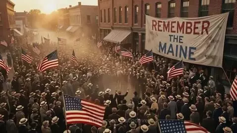 High-angle view of a large crowd waving American flags on a street lined with brick buildings, banner reads 'REMEMBER THE MAINE'.