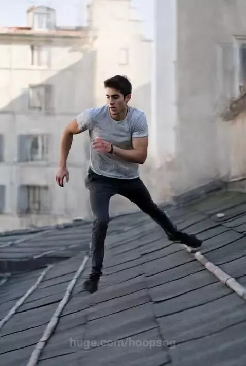 Parkour athlete mid-jump between urban rooftops, showcasing agility and balance against a city skyline.