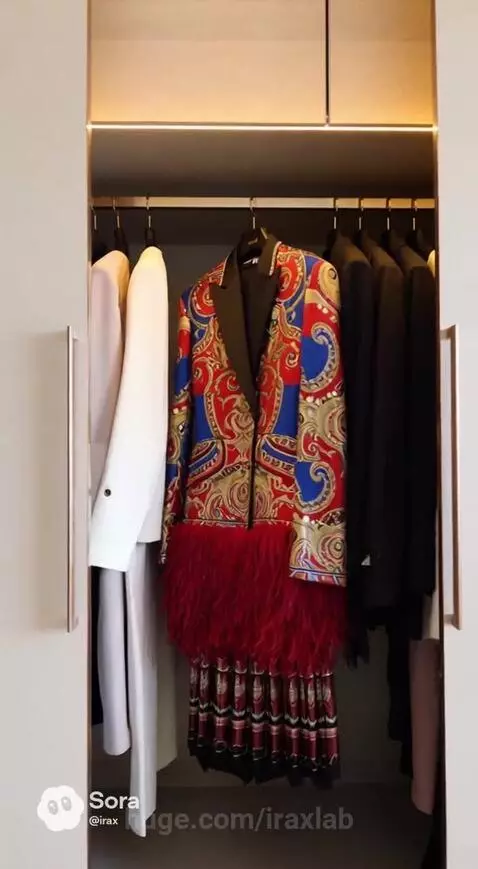 Woman in black dress and boots opens a modern closet, revealing a vibrant patterned jacket.