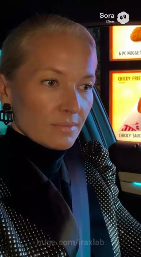 Woman in sparkly jacket at a drive-thru at night ordering food.