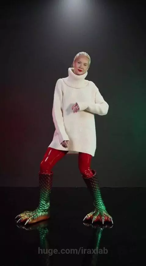 Woman with red lipstick and green and red scaly monster boots dancing.
