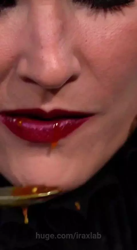 Woman in elaborate outfit eating orangutan testicles from a can labeled 'OURANGUTANG TESTICLES SAMARIND GLAZE'.