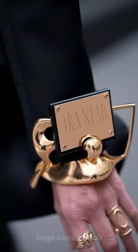 Woman with blonde hair in a black dress with puffed sleeves and golden cuffs, followed by a winged figure.