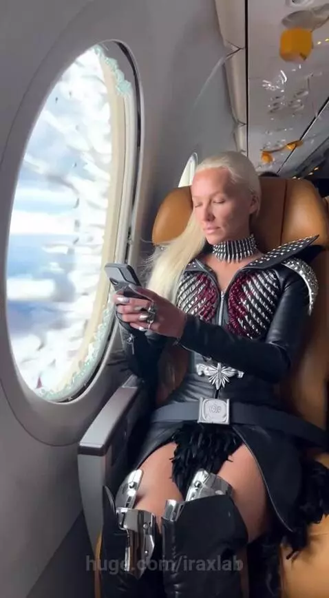 Woman in a warrior outfit sits in a plane with a shattered window and debris flying past, preparing for impact.