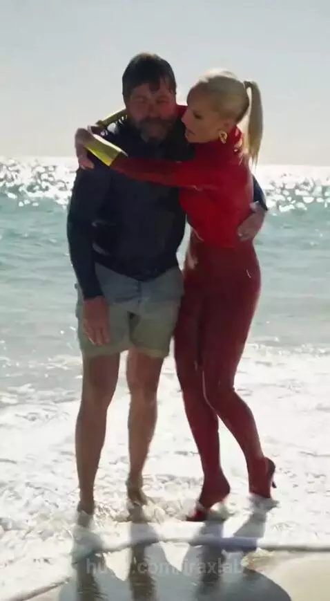 Lifeguard in a red and gold suit swimming to rescue a man in the ocean.