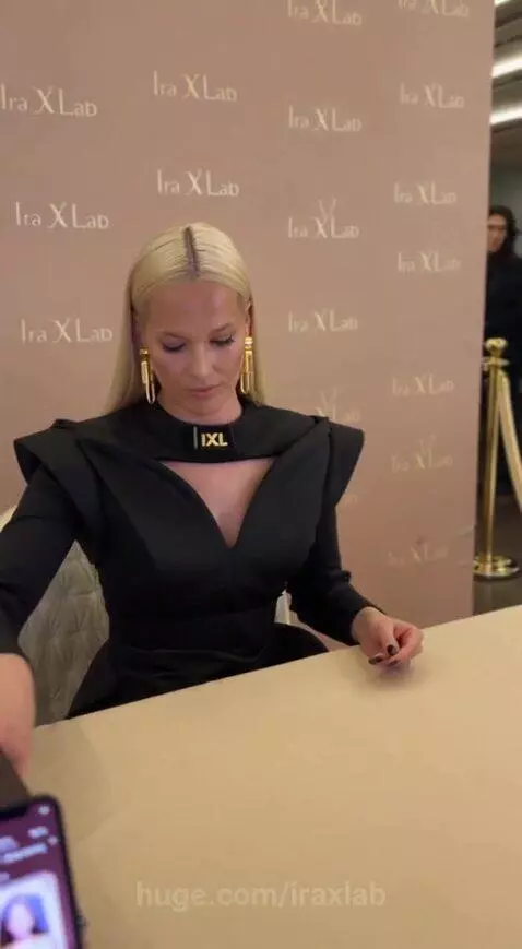 Woman in black dress signing a magazine with a golden pen at an event with 'IXL' branding.