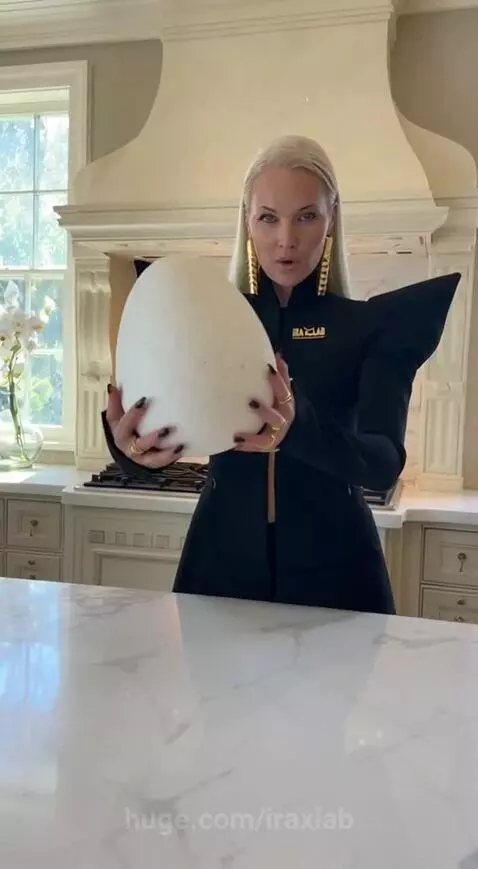 Woman in blazer unboxing a large white egg to reveal a gold-wrapped chocolate egg inside.