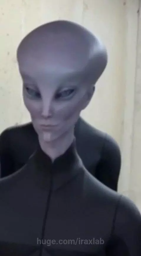 Woman in a basement with six grey alien figures in black bodysuits, some standing behind her.
