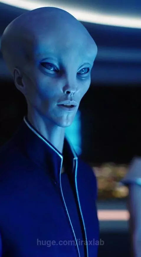 Grey-skinned alien in a blue suit and human-like woman in a black dress in a futuristic room with a city view.