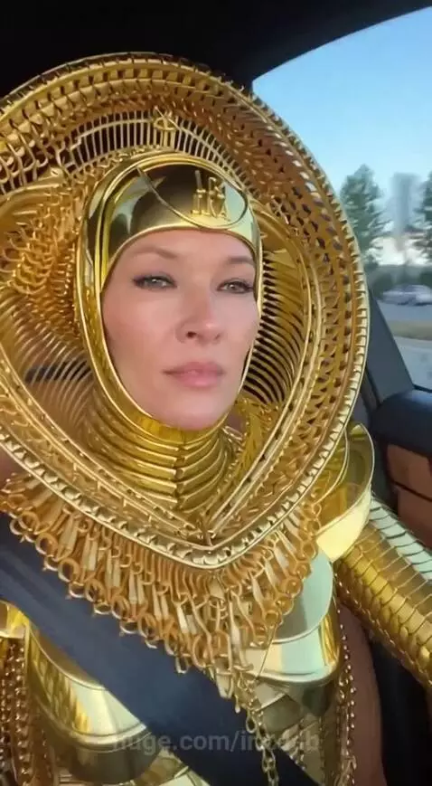 Woman wearing a detailed full-body golden costume and headpiece, sitting in a gold car.