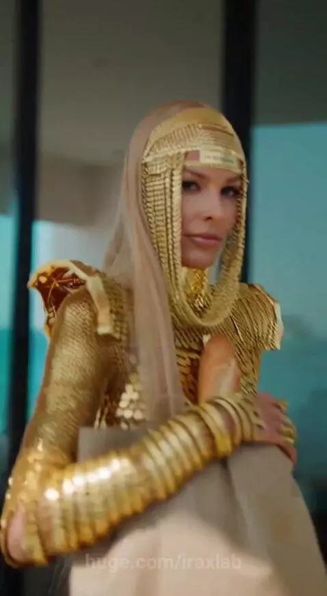 Woman in a futuristic golden scale-like outfit and headpiece exiting a golden car with a grocery bag.