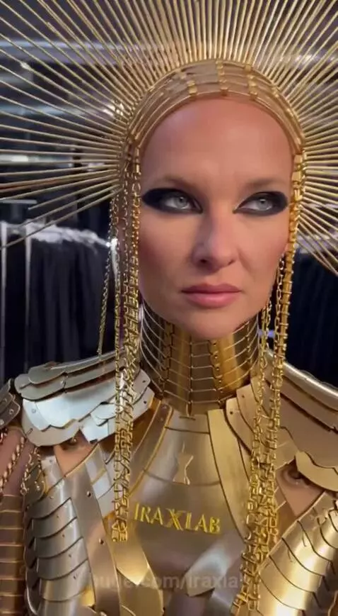 Woman in elaborate golden armor costume with sunburst headpiece backstage at Paris Fashion Week.
