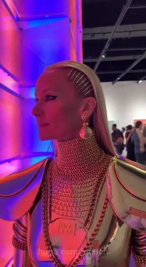 Woman in full-body golden futuristic armor suit with 'IRA LAB' on chest plate at Art Basel.
