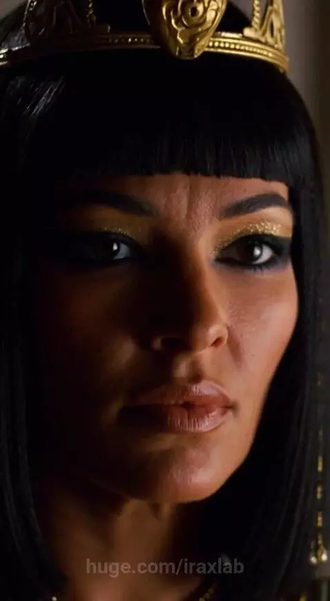 Woman in elaborate ancient Egyptian attire resembling Cleopatra with a golden cobra headpiece, standing near a man in Roman armor.