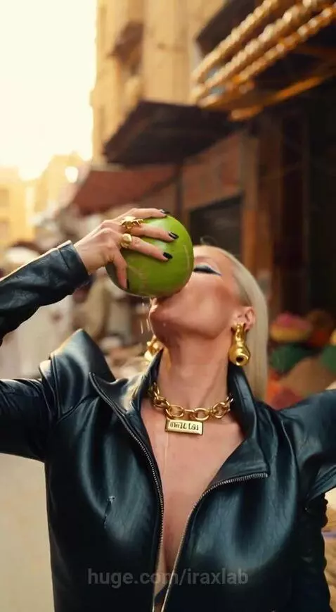 Woman in leather dress and boots holding a knife and a coconut in an outdoor market.
