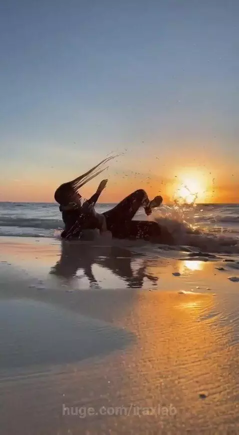 Woman in black outfit splashing water in the ocean at sunset, golden light reflecting.