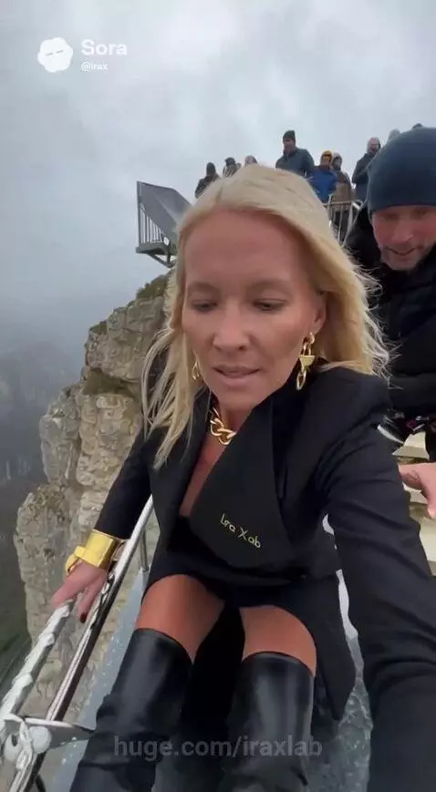 Woman in blazer and boots on a metal slide built into a misty canyon cliff, smiling.