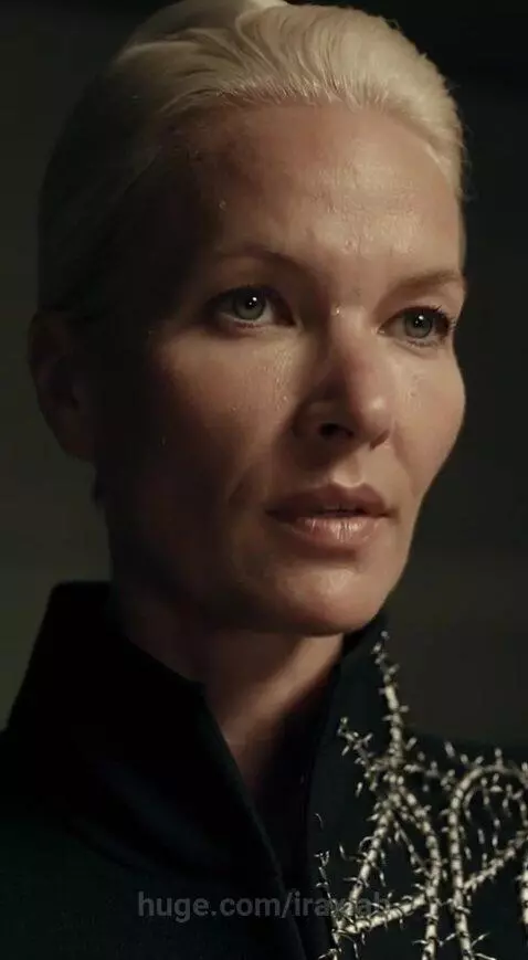 Woman in a structured jacket with thorny lapel undergoing an interrogation, wires attached to her arm connected to a polygraph machine.