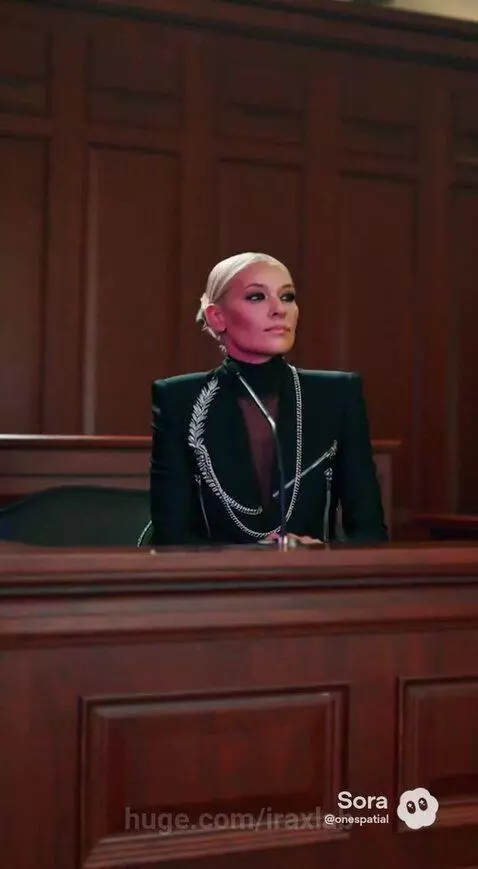Woman in a black suit and turtleneck performing an energetic K-pop dance in a brightly lit courtroom.