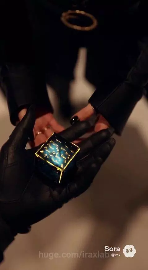 Silhouette of a winged figure handing a glowing blue cube to a woman in a luxurious room at night.