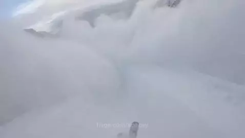 First-person view of a skier descending a snow-covered mountain, kicking up large plumes of powder.