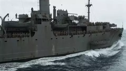 World War II troop transport ship with many soldiers on deck, sailing through choppy ocean waves under an overcast sky.