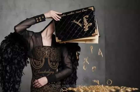 Woman with an ornate black book for a head, wearing a black and gold dress, with golden letters floating around her.