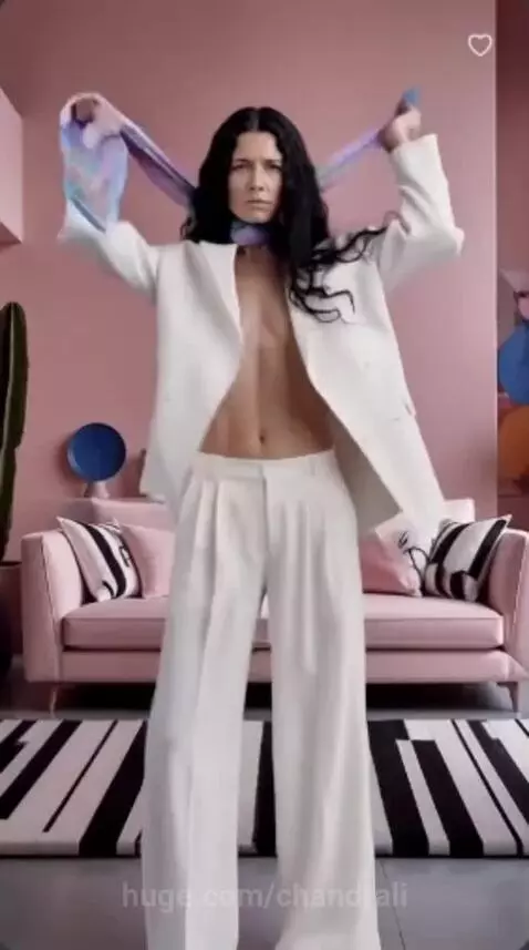 Woman with long dark hair in a white blazer and pants dancing in a pink room with abstract art.
