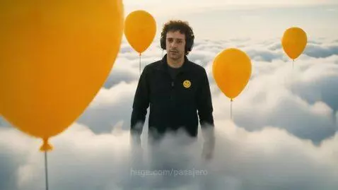 Man with smiley face patch on jacket, dancing and floating amidst yellow balloons and guitars.