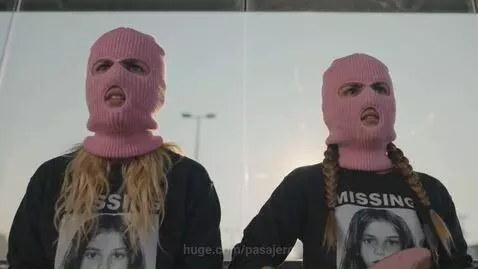 Two women in pink balaclavas perform on a moving bus in Mexico City, with cityscapes in the background.