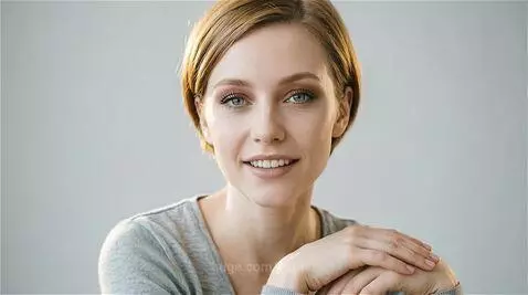 Close-up portrait of a woman with short blonde hair and blue eyes, smiling then looking directly at the camera.