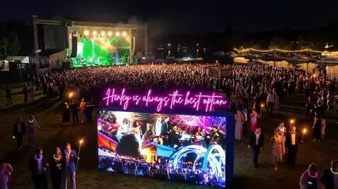 Elevated view of Henley Festival at night with a band performing on stage, LED screen, neon sign, and illuminated water.