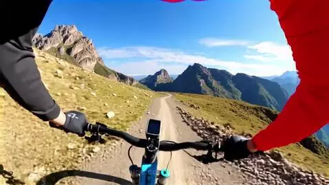 First-person view of mountain biking on a dirt trail with vast, sunny mountains and blue sky in Peru.