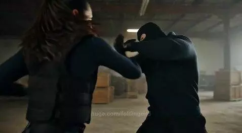 Woman in tactical gear performing martial arts moves during a fight in a warehouse.
