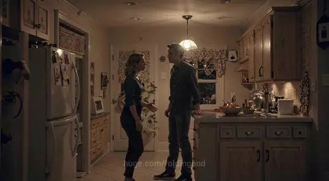 A man and woman in a kitchen arguing intensely, with the woman confronting the man about his car being seen downtown.
