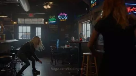 Two women fighting violently in a dimly lit bar, one with blonde hair, the other with red hair, with a broken barstool and scattered glasses.