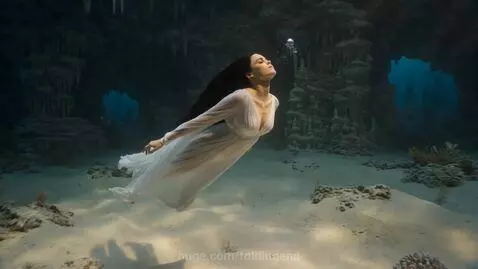 Woman transforming into a mermaid with a shimmering blue and purple tail in an underwater cave with light shafts.