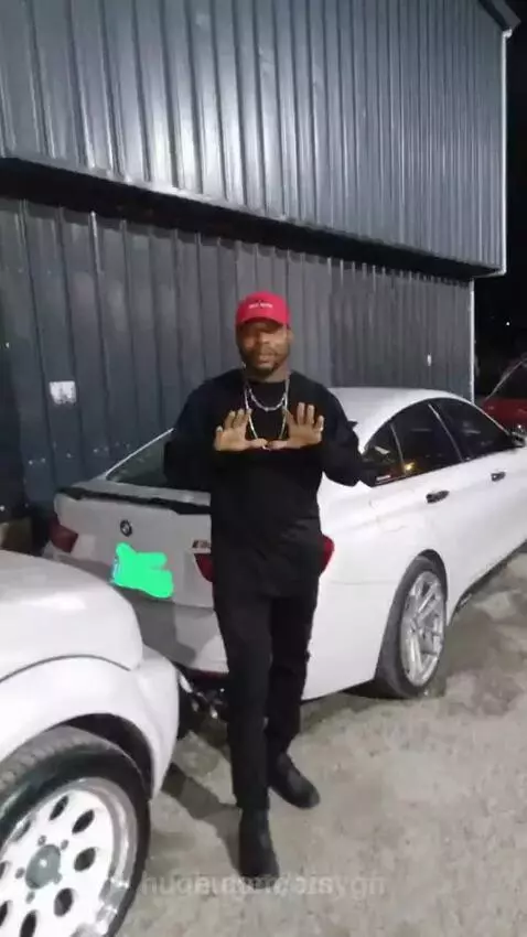Man in red cap walking towards a modern building at night, greeted by smiling people inside.
