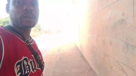 Man in Chicago Bulls jersey stands under a concrete overpass, looking at the camera and smiling.