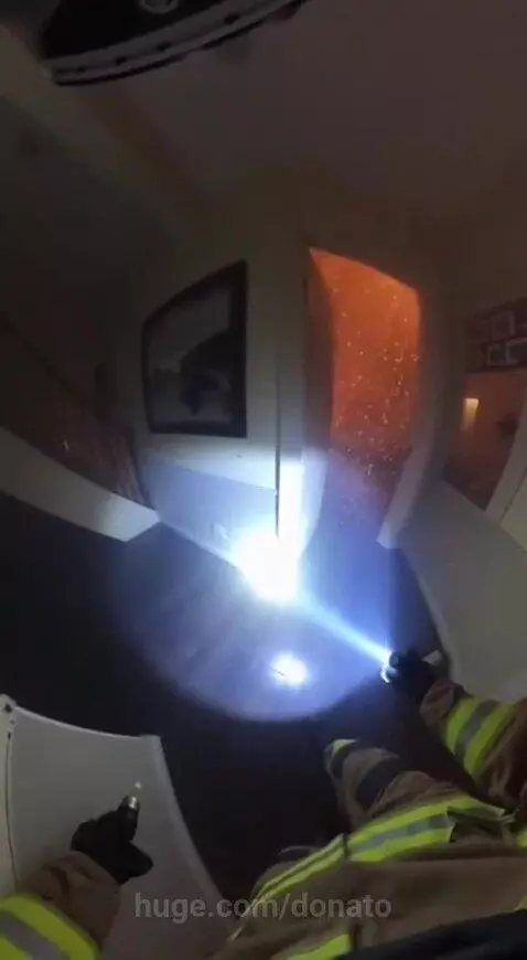 Firefighter carrying a child out of a smoke-filled burning house towards a ladder.