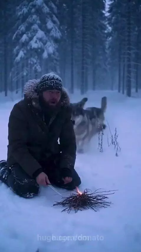 Man kneeling in snowy forest, smiling as friendly wolves surround him and nuzzle him.