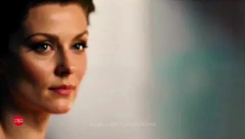 Woman in a dark blue gown on a spotlighted opera stage, singing.