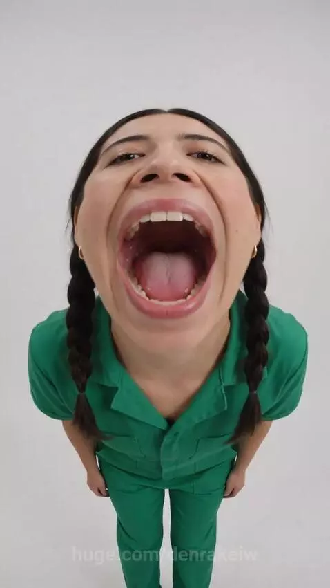 Woman in green jumpsuit with mouth wide open, showing tongue, with LOUDMOUTH! candy bar.