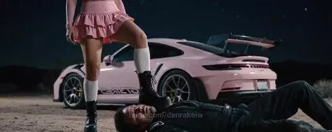 Woman in pink corset and thigh-high stockings steps on a man after a car race crash.