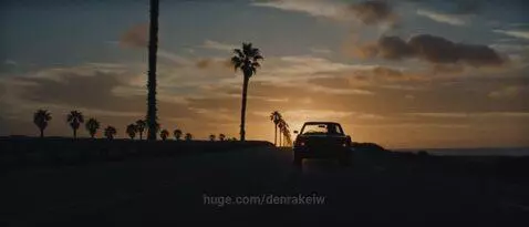 Woman in bikini top and denim jacket walking on a beach at sunset with a man.
