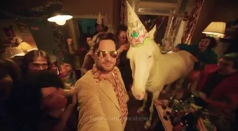 Man in 70s suit takes selfie with horse wearing party hat and sunglasses at a lively party.